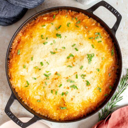 Overhead view of healthy shepherd's pie in a baking dish. A drink, oven mitts, rosemary, napkin, plates, and forks on the side.