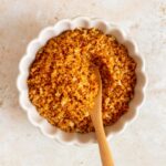 Overhead view of a beige bowl with toasted breadcrumbs with a wooden spoon inside.