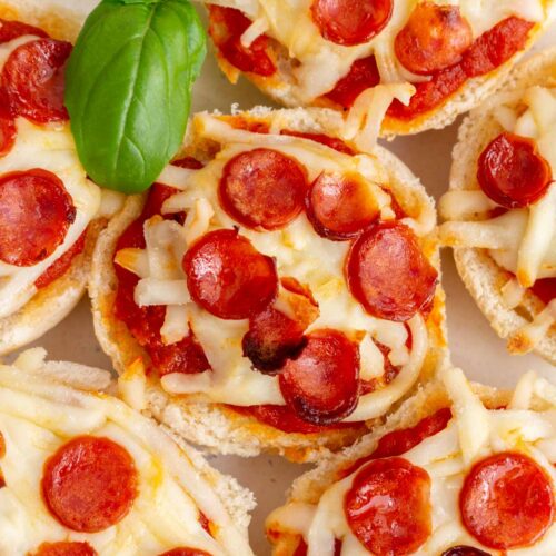 Overhead view of mini pizza bagels topped with mini pepperoni with fresh basil.