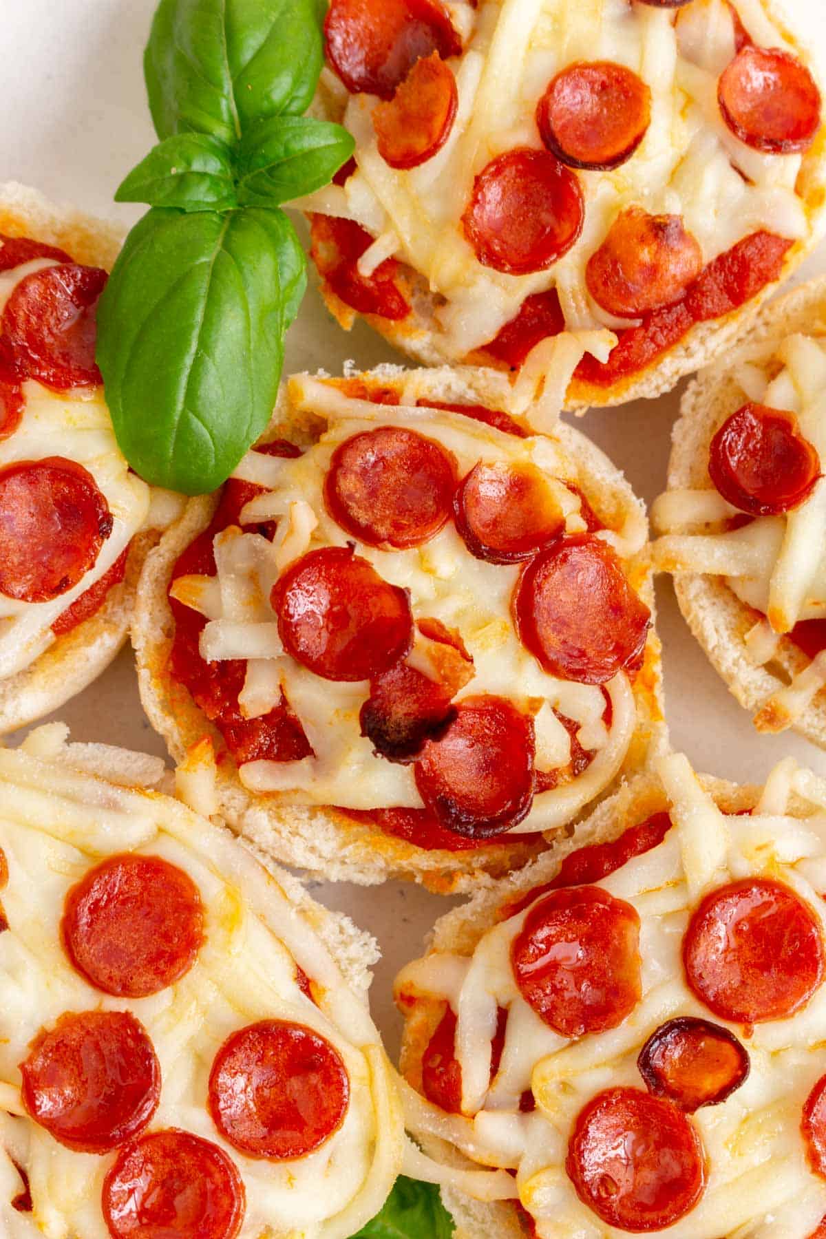 Overhead view of mini pizza bagels topped with mini pepperoni with fresh basil.