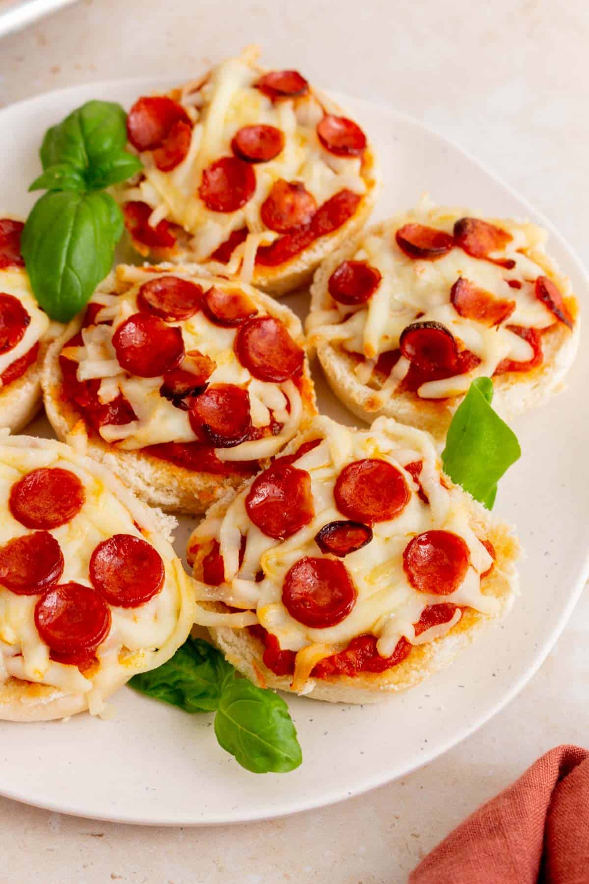 A plate of mini pizza bagels with fresh basil.