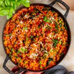 Overhead view of a large skillet of sausage orzo topped with shredded parmesan and basil.