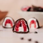 A profile view of the interior of a cut chocolate covered raspberry. Two more in the background, out of focus.