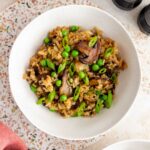 A bowl of mushroom fried rice topped with green onions. Garlic, salt and pepper shakers, and another bowl off to the side.