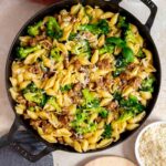 Overhead view of a skillet of sausage and broccoli pasta topped with parmesan and basil.