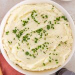Overhead view of a large bowl of sour cream mashed potatoes with chives and black pepper on top.