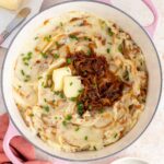 Overhead view of caramelized onion mashed potatoes in a pot topped with butter, chives, and more caramelized onions.