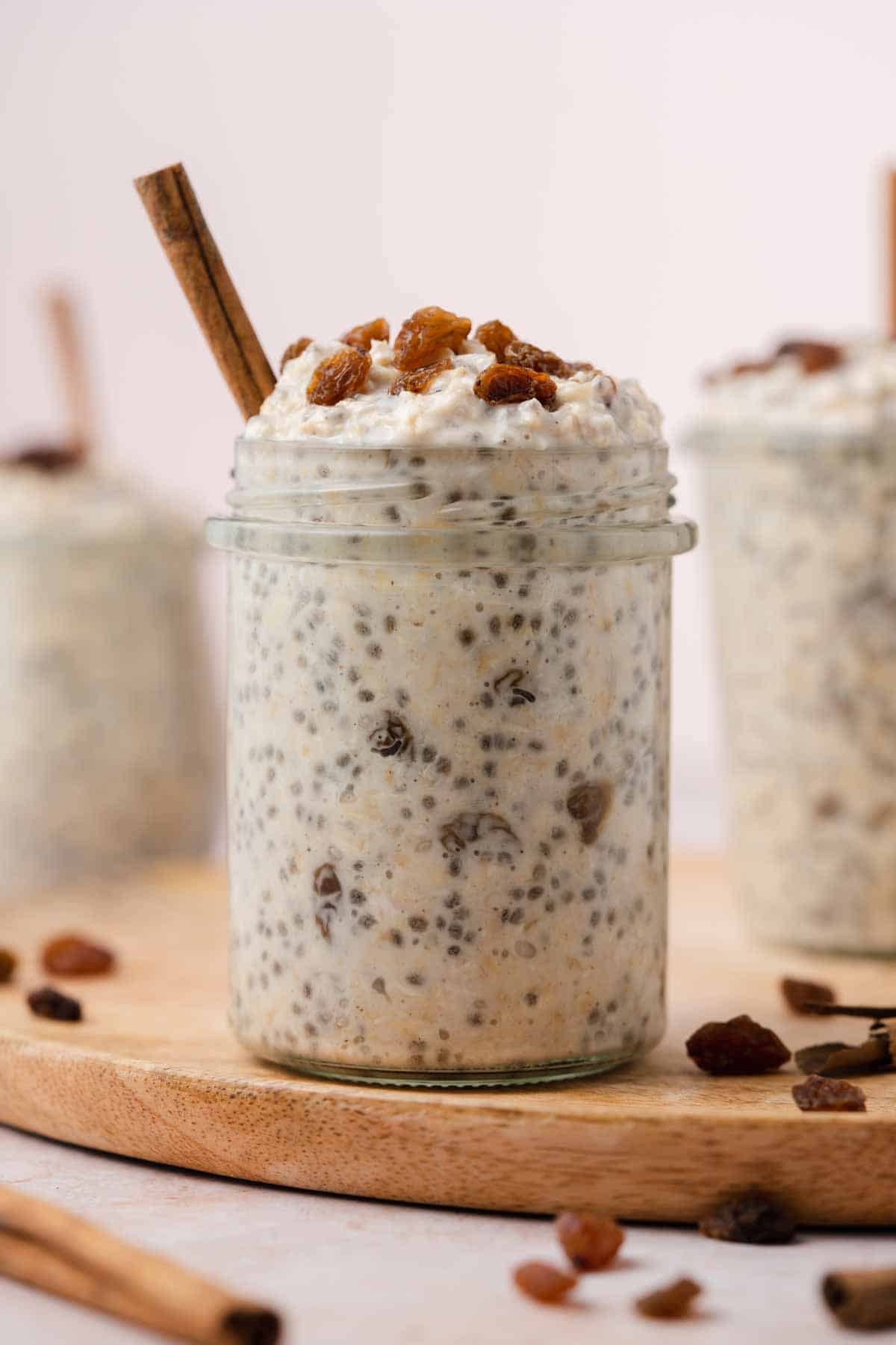 A profile view of a jar of cinnamon raisin overnight oats topped with raisins and cinnamon stick stuck inside.