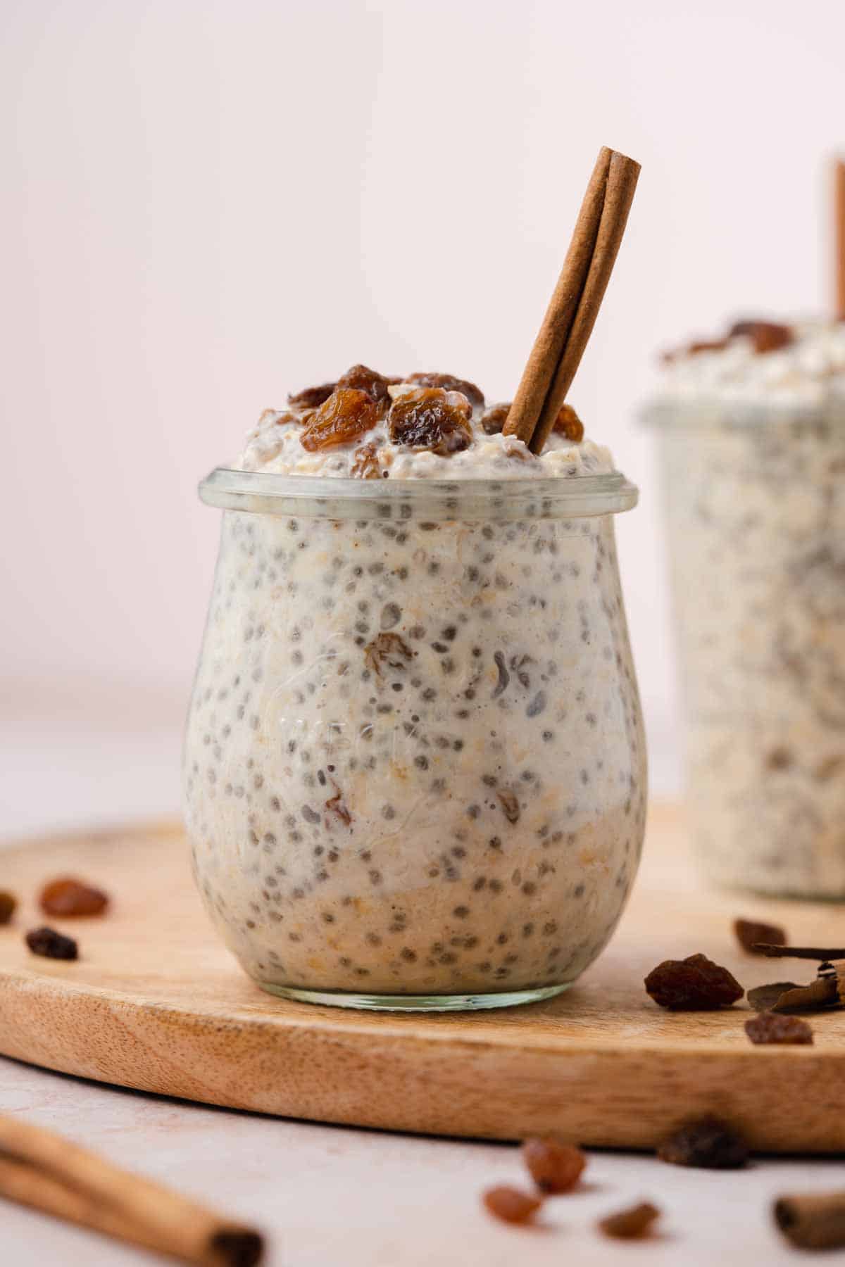 A jar of cinnamon raisin overnight oats with raisins on top and a cinnamon stick.