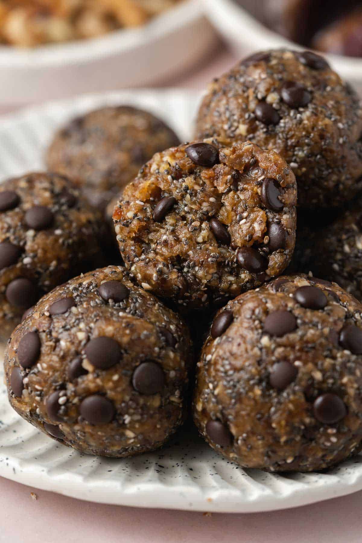 A close up view of a plate full of nut date balls with one with a bite taken out.