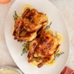 Overhead view of a platter with two air fryer cornish game hens surrounded by lemon slices and fresh thyme.