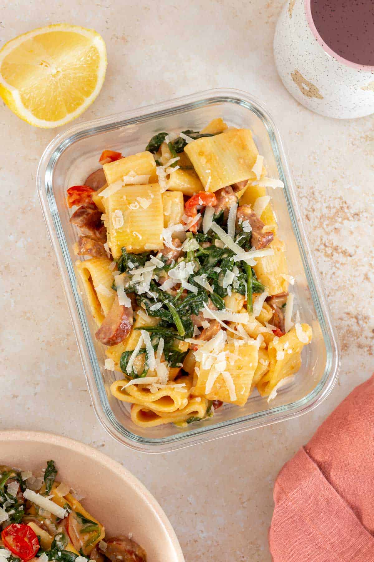 Overhead view of chorizo and spinach pasta in a meal prep container topped with fresh parmesan.