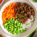 Overhead view of a bowl of rice with firecracker beef, edamame, and carrots.