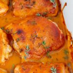 A close up view of the honey dijon mustard chicken thighs in a baking dish, topped with fresh thyme.