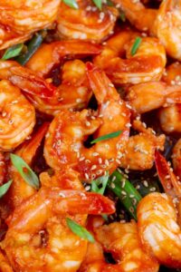 Close up view of ketchup shrimp with green onions and toasted sesame seeds.