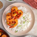 A plate of rice with ketchup shrimp on half of it.