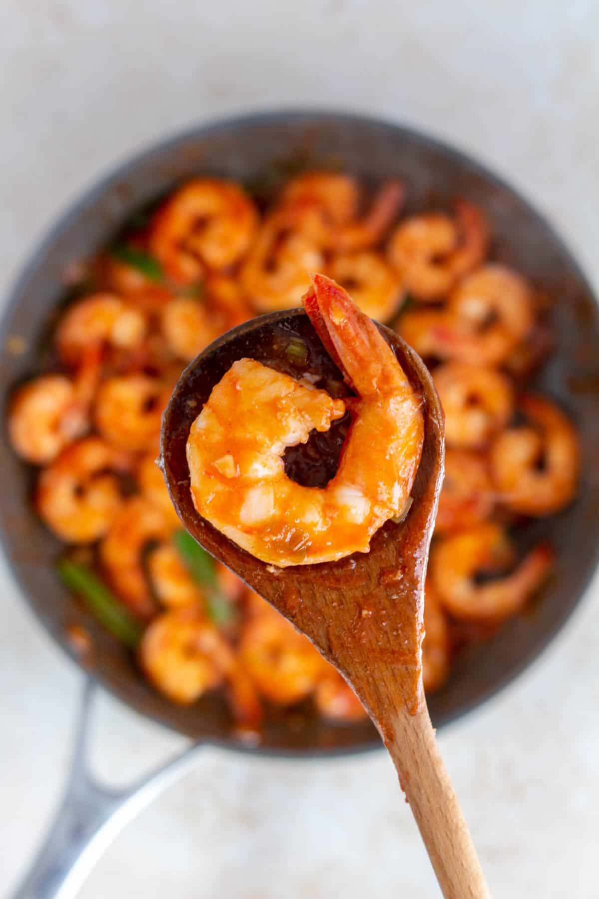 A wooden spoon holding up a ketchup shrimp from a skillet.