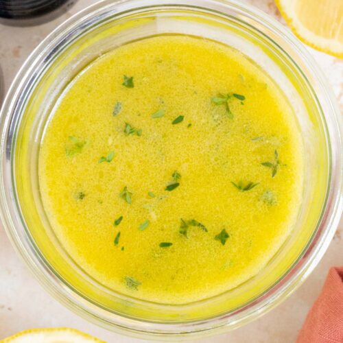 Overhead view of a jar of lemon thyme vinaigrette. Cut lemons off to the side with a pepper grinder.