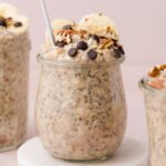 A jar of banana bread overnight oat on a marble coaster with a spoon inside.