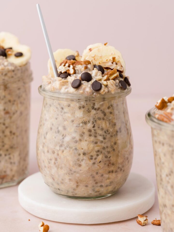 A jar of banana bread overnight oat on a marble coaster with a spoon inside.