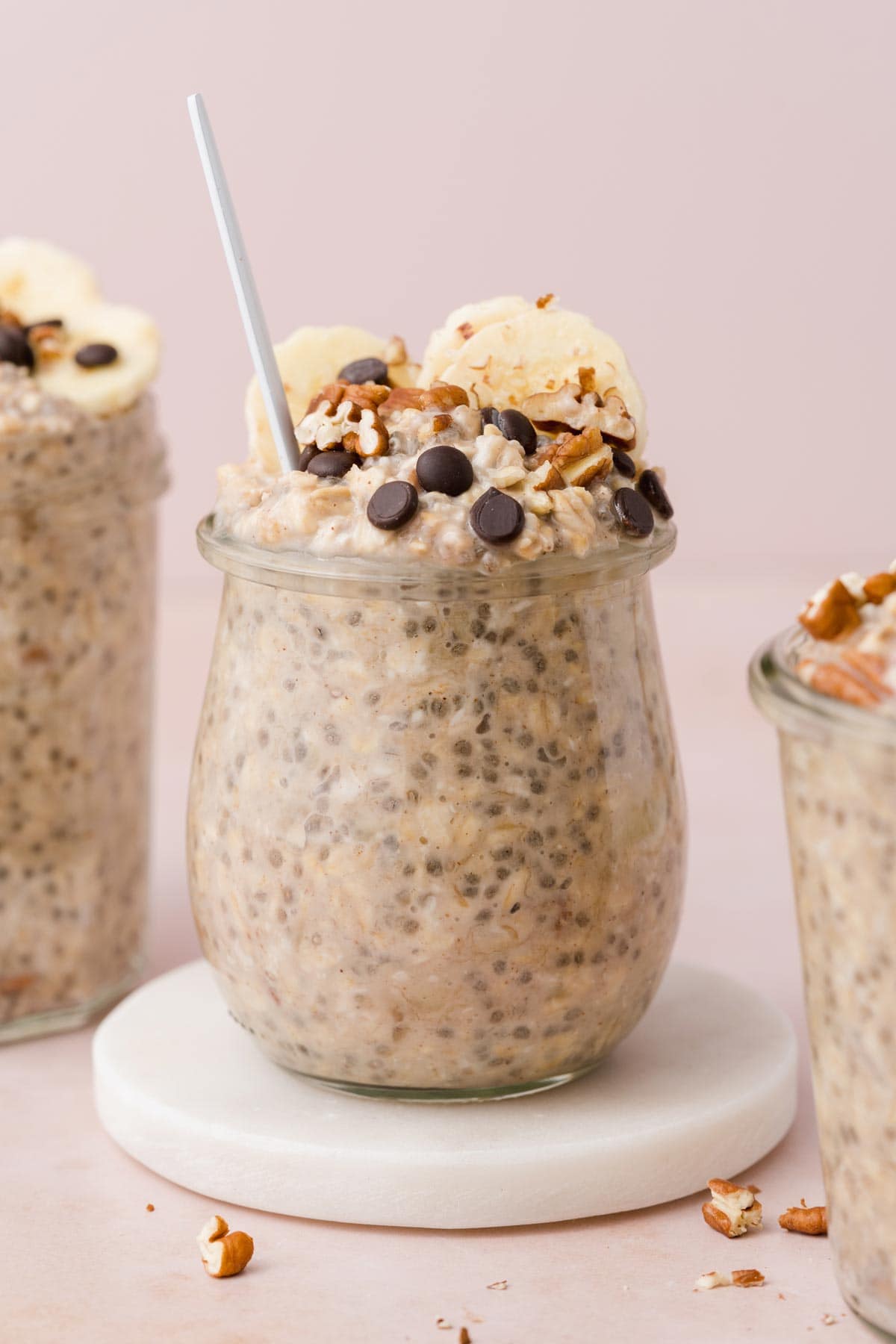 A jar of banana bread overnight oat on a marble coaster with a spoon inside.