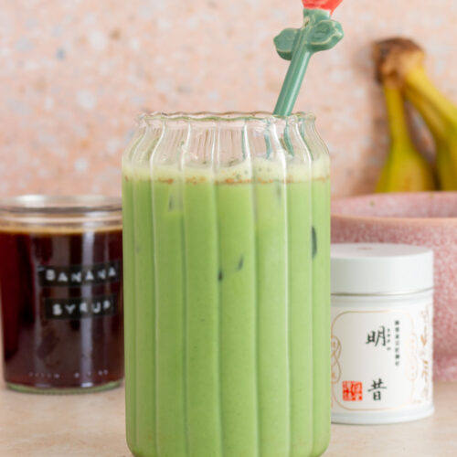 A glass of banana bread matcha with a floral stir stick.