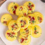 Overhead view of a platter of cottage cheese egg bites with bacon bits and chives.