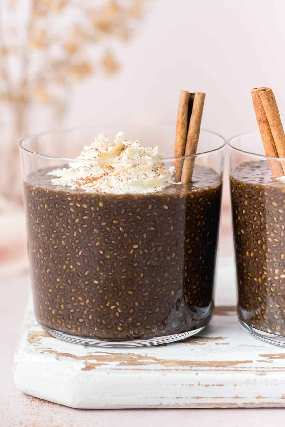 A glass of gingerbread chia pudding topped with whipped cream and a cinnamon stick.