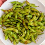 A bowl of sesame edamame topped with flaky salt and toasted sesame seeds.