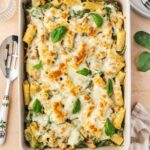 Overhead view of a chicken spinach and artichoke pasta bake in a white baking dish.