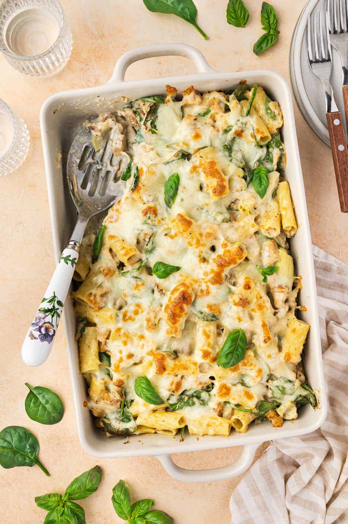 Overhead view of a spinach and artichoke pasta bake with a serving taken out and a serving spoon tucked into it.