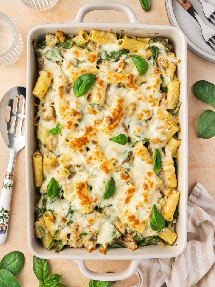 Overhead view of a chicken spinach and artichoke pasta bake in a white baking dish.