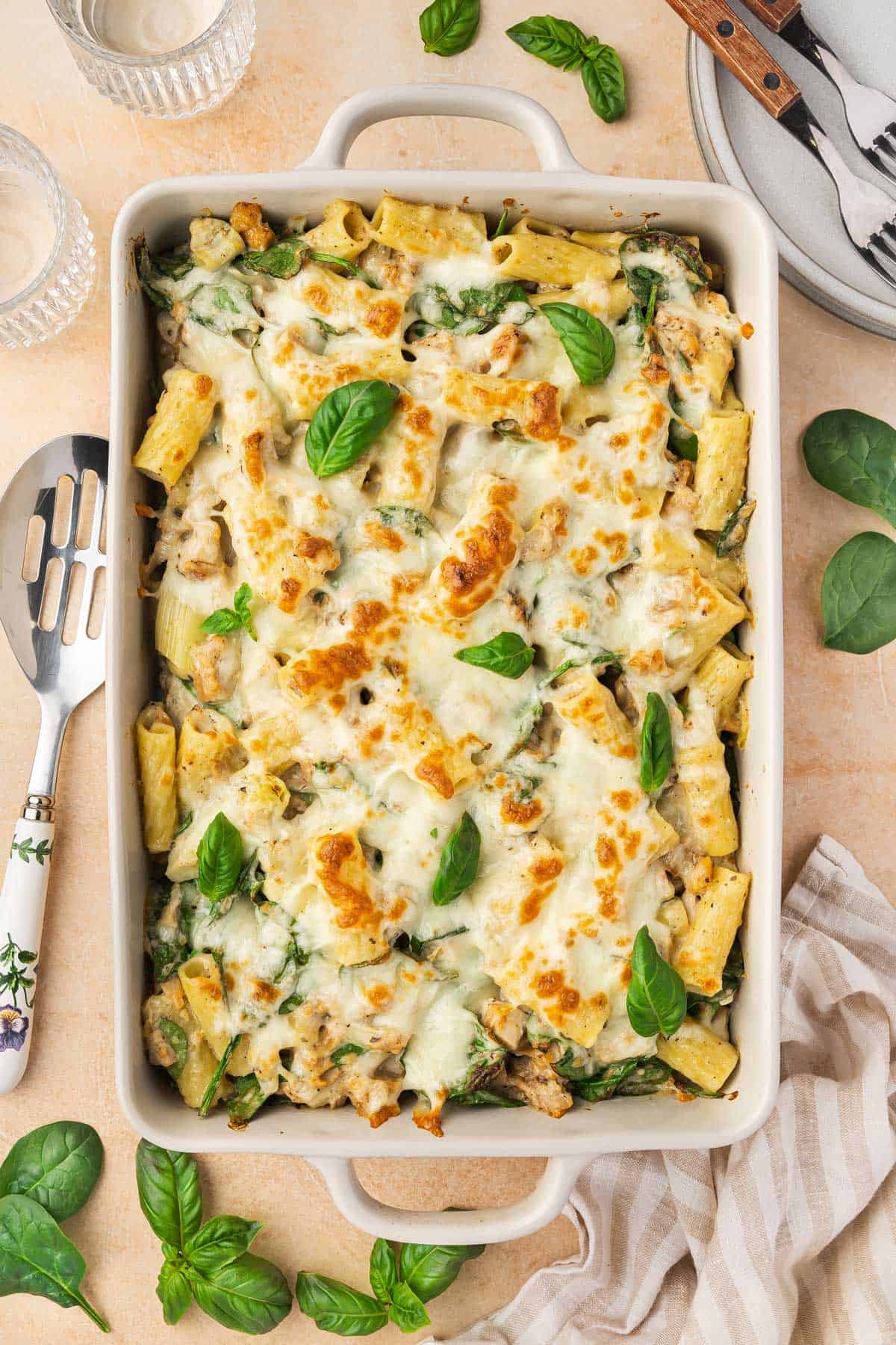 Overhead view of a chicken spinach and artichoke pasta bake in a white baking dish.