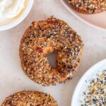 Overhead view of an cottage cheese bagel with more around it along with cream cheese and everything but the bagel seasoning.