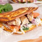 A close up of cottage cheese flatbread folded in half with chicken, spinach, tomato, and onion inside.