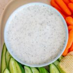 A bowl of cottage cheese ranch dip with some cucumbers, chips, and baby carrots around it.