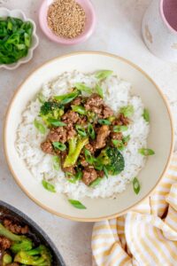 Overhead view of ground beef and broccoli over rice in a bowl garnished with sesame seeds and green onions.
