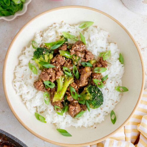 Overhead view of ground beef and broccoli over rice in a bowl garnished with sesame seeds and green onions.