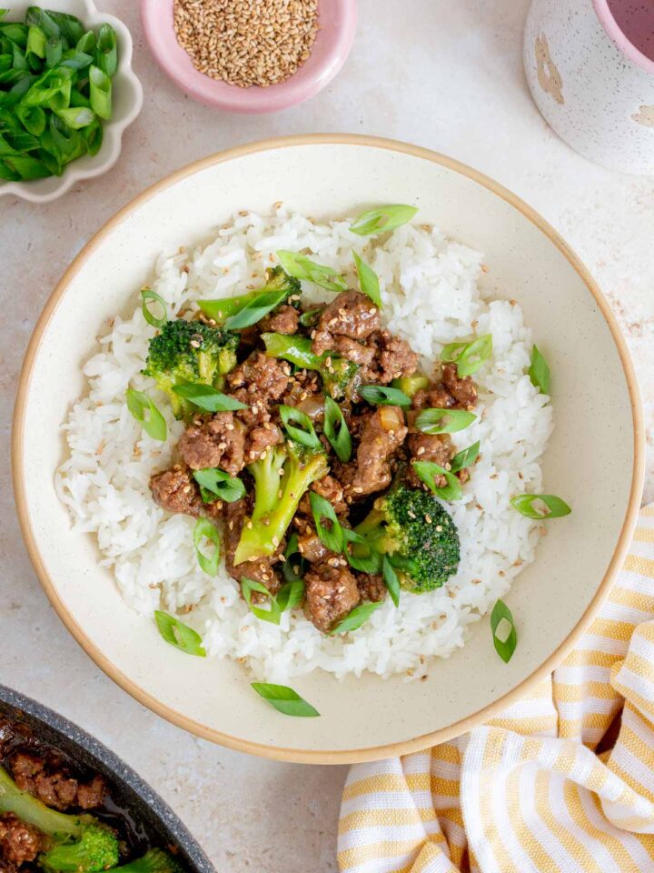 Overhead view of ground beef and broccoli over rice in a bowl garnished with sesame seeds and green onions.