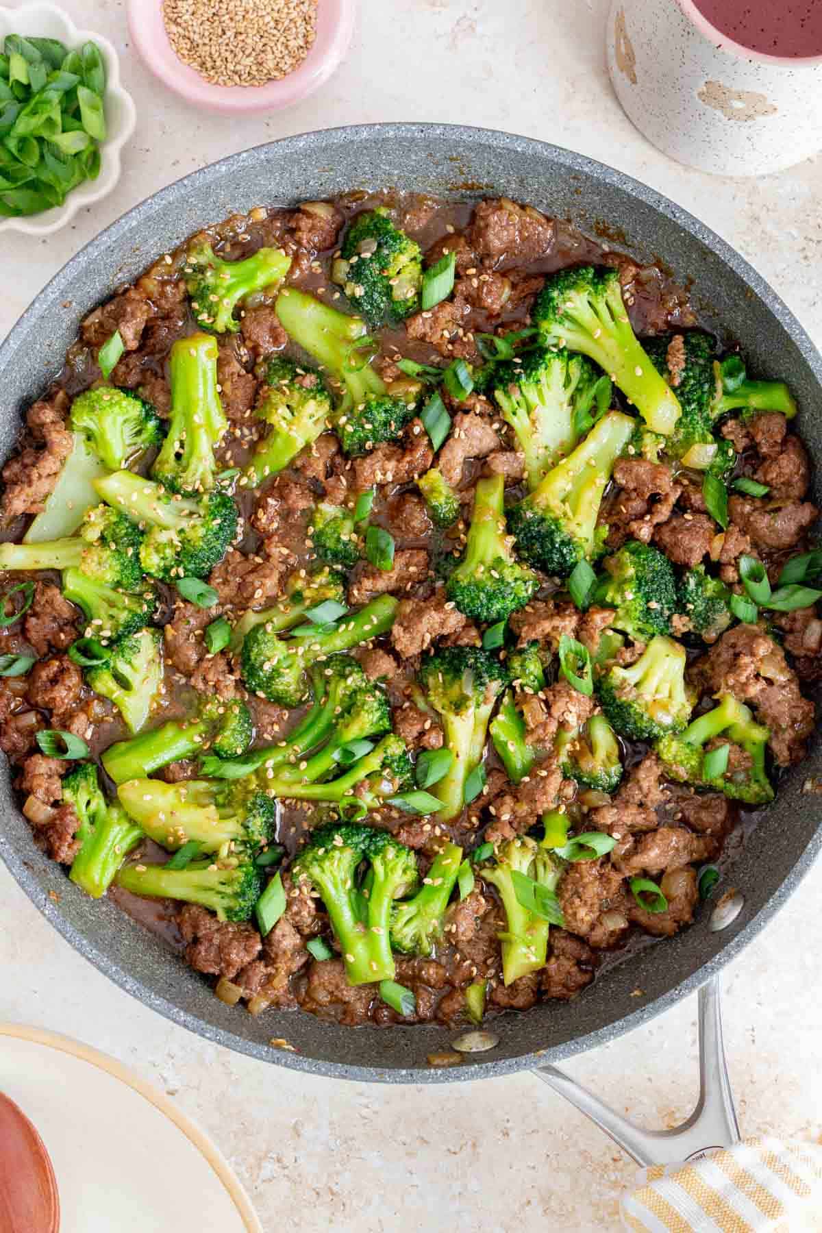 Overhead view of a skillet of ground beef and broccoli with green onions and sesame seeds.