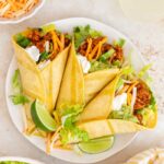 An overhead view of a plate with three ground turkey tacos with sour cream, guacamole, shredded cheese, and lettuce. Lime wedges on the plate.