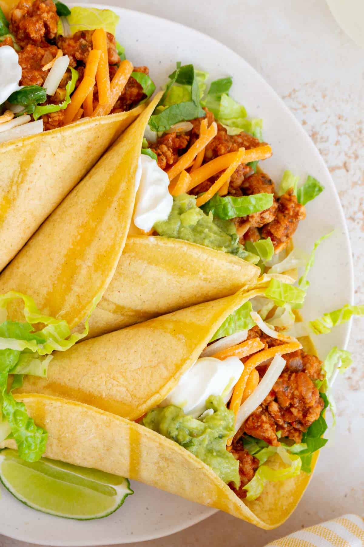 A close up overhead view of three ground turkey tacos with sour cream, guacamole, shredded cheese, and lettuce.