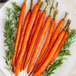 A white platter of maple glazed carrots with some herbs surrounding it.
