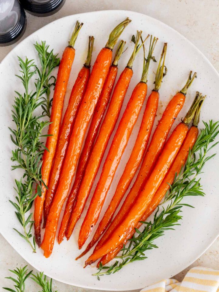 A white platter of maple glazed carrots with some herbs surrounding it.
