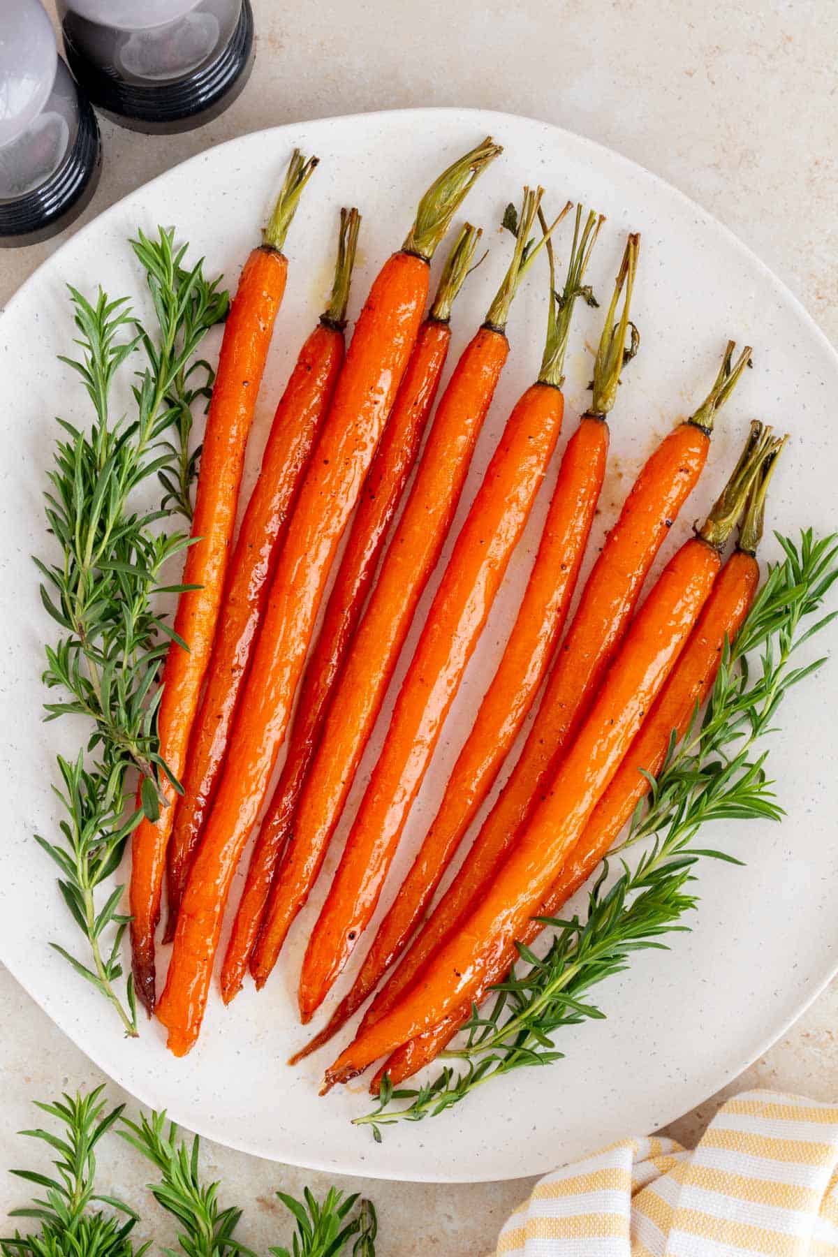 A white platter of maple glazed carrots with some herbs surrounding it.