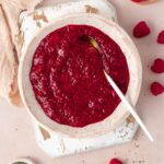 Overhead view of a bowl of homemade raspberry chia jam with a spoon. Chia seeds and fresh raspberries scattered around and in bowls.