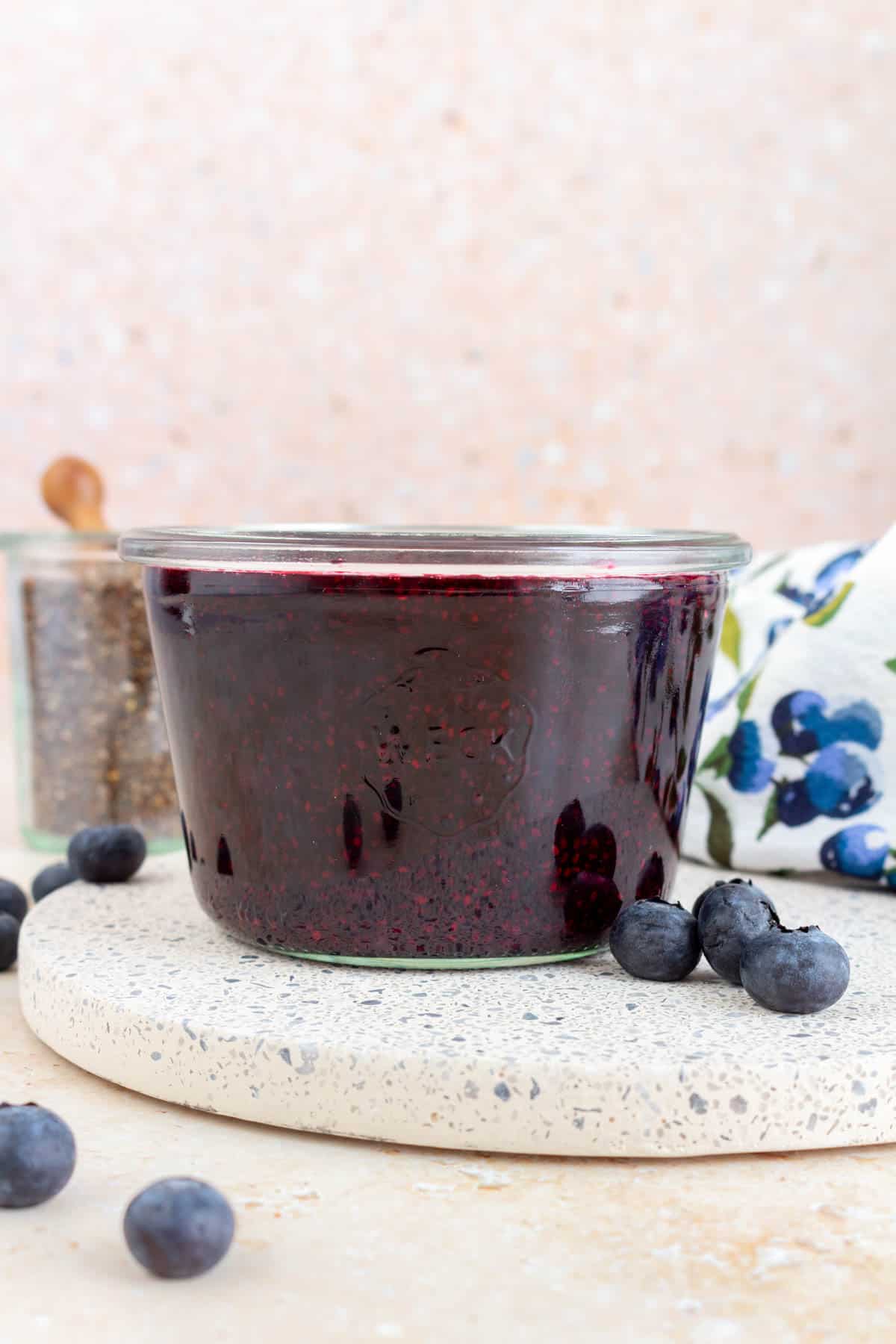 A jar of blueberry chia jam with fresh blueberries scattered around.