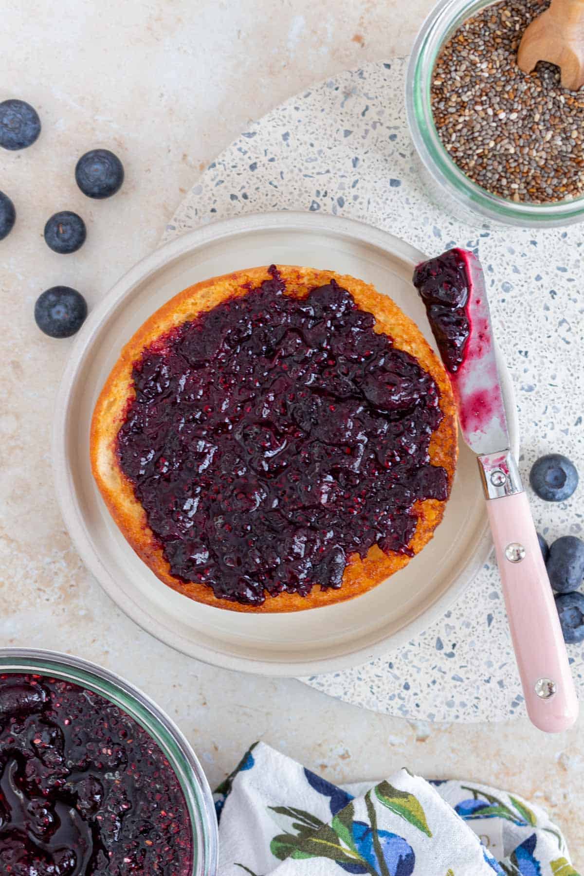 Overhead view of blueberry chia jam spread on a toasted bagel on a plate.