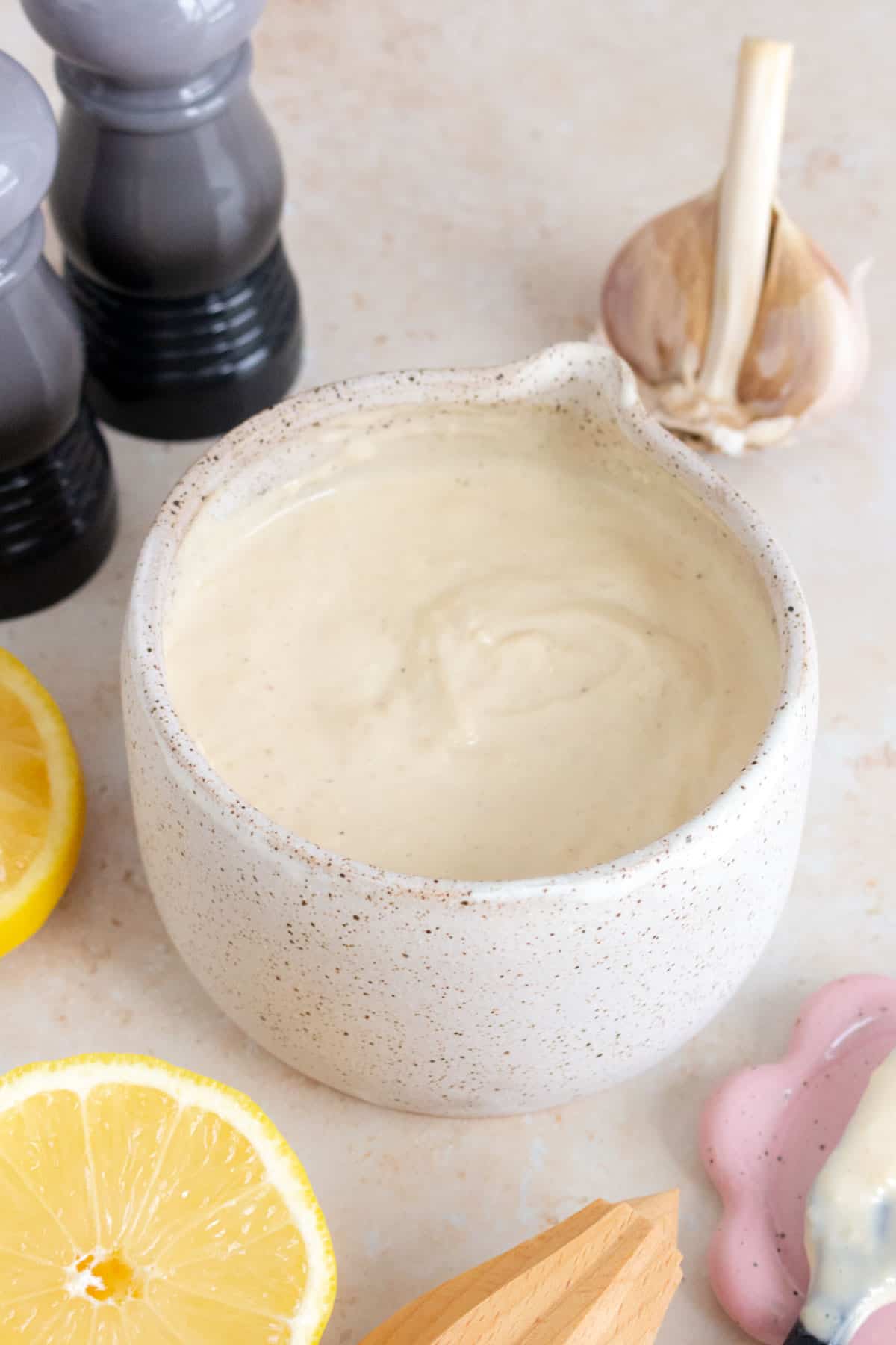 A bowl of homemade caesar salad dressing. Lemon, garlic, salt, and pepper surrounding the bowl.