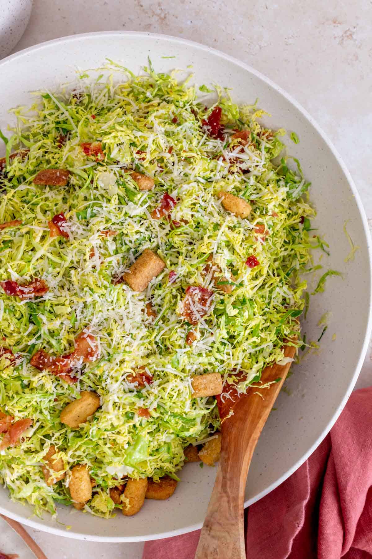 Overhead view of shaved brussels sprouts caesar salad in a large serving bowl with a wooden spoon.